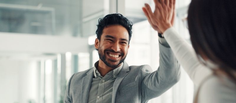 High-Five zwischen zwei Personen als Symbol für erfolgreiche Zusammenarbeit, um Marktanteile zu steigern und Neukunden zu gewinnen.