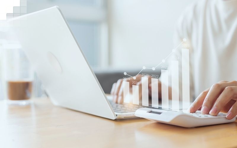 Analyse von Geschäftszahlen am Laptop mit Taschenrechner und wachsendem Diagramm als Symbol für Umsatz und Profit steigern.